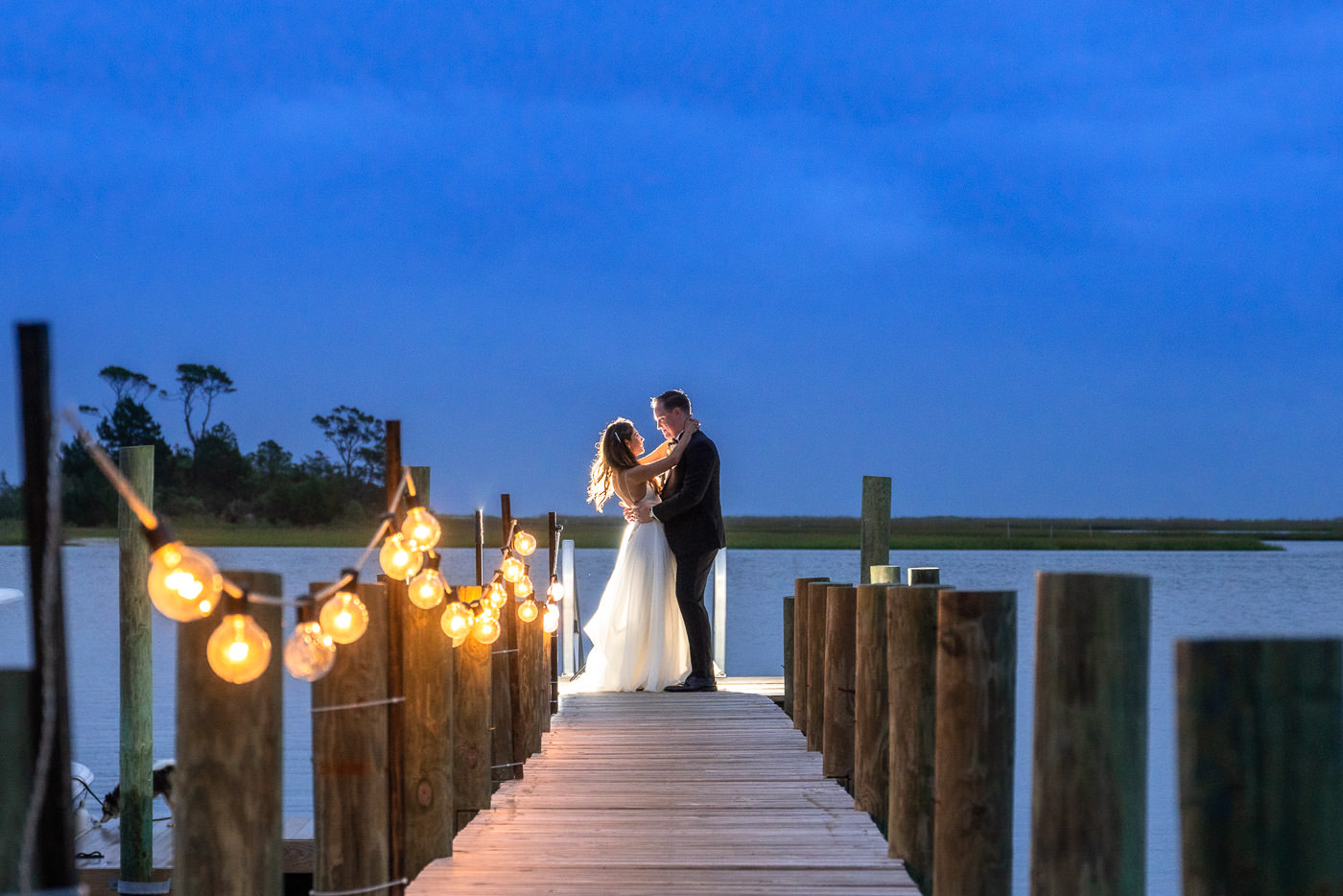 Bride and groom embracing at the end of a boat dock - intercoastal waterway - twilight wedding photo - edison lighting - wedding dress - black tux - wedding photo idea - wilmington nc wedding wedding photographers - chris lang photography